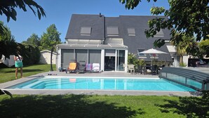 Una piscina con sillones de descanso y un porche cubierto.