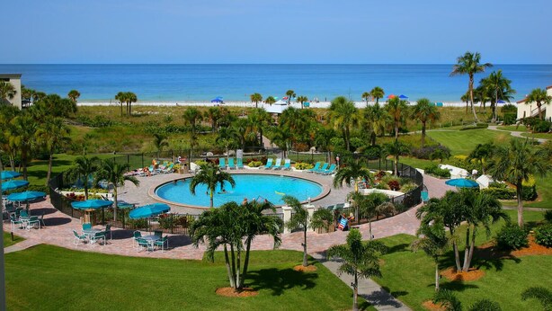 Ein Resort mit einem zentral gelegenen Pool, Liegestühlen und Palmen.