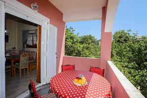 A balcony with a red table and chairs, a fruit bowl, and a view of greenery. - Alice & Teo Houses (Corfu)