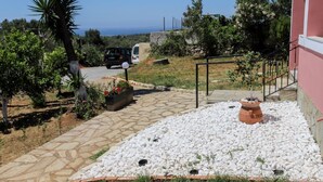 A paved pathway leading to a building with a stone roof, surrounded by white pebbles and greenery. - Alice & Teo Houses (Corfu)