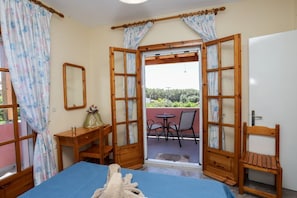 A bedroom with a bed, a wooden desk, a chair, a mirror, and an open door leading to a balcony with a table and chairs. - Alice & Teo Houses (Corfu)