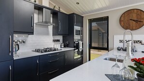 A modern kitchen with dark cabinets, a white countertop, stainless steel appliances, and a wooden clock on the wall.