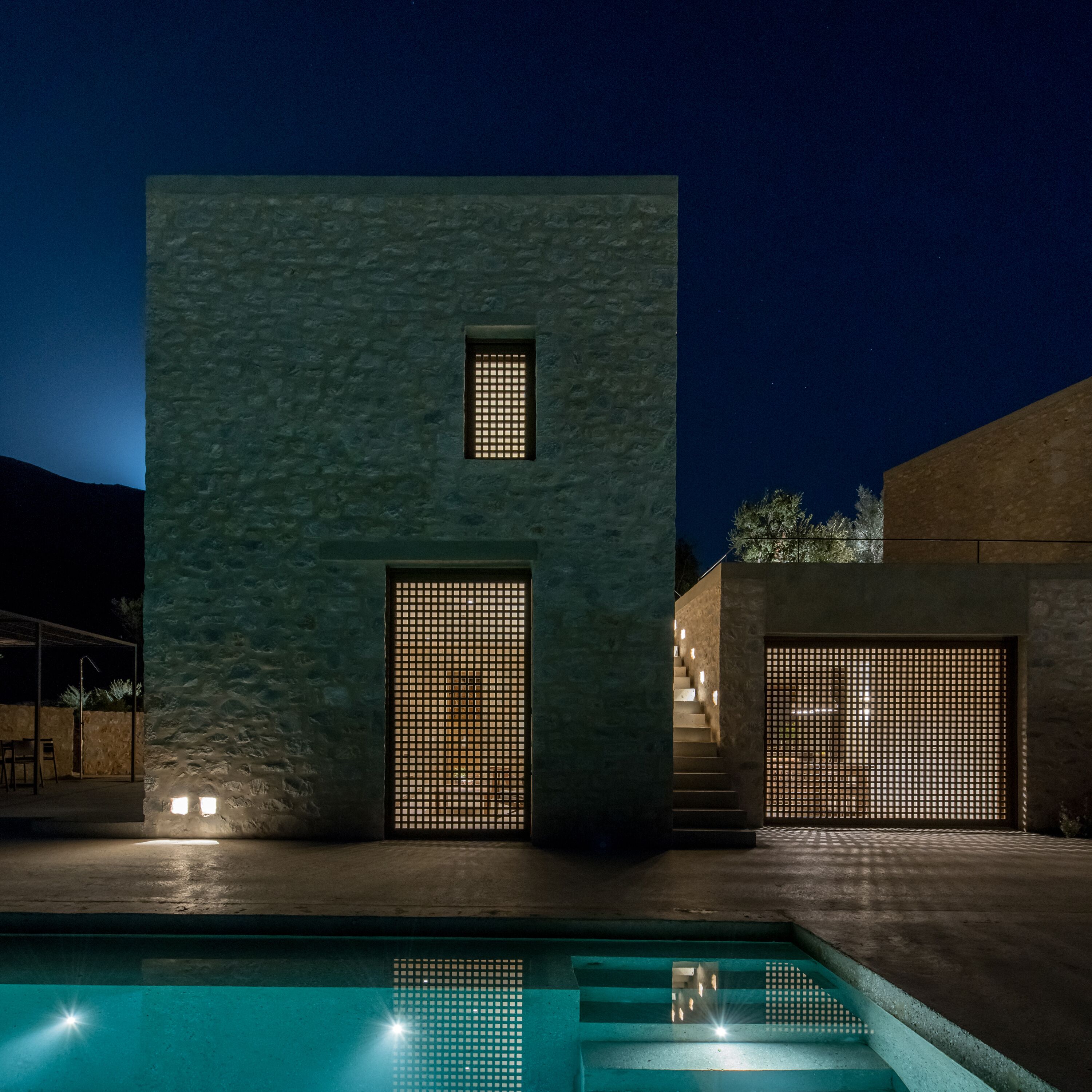 A modern building with a pool, featuring a textured facade and two large windows with grid patterns.