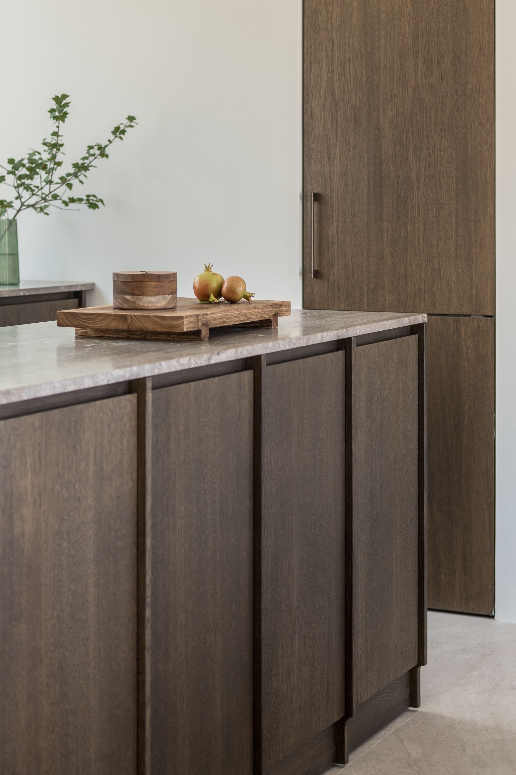 Una cocina con armarios de madera oscura, encimera de mármol y tabla de madera con manzanas y cebollas.
