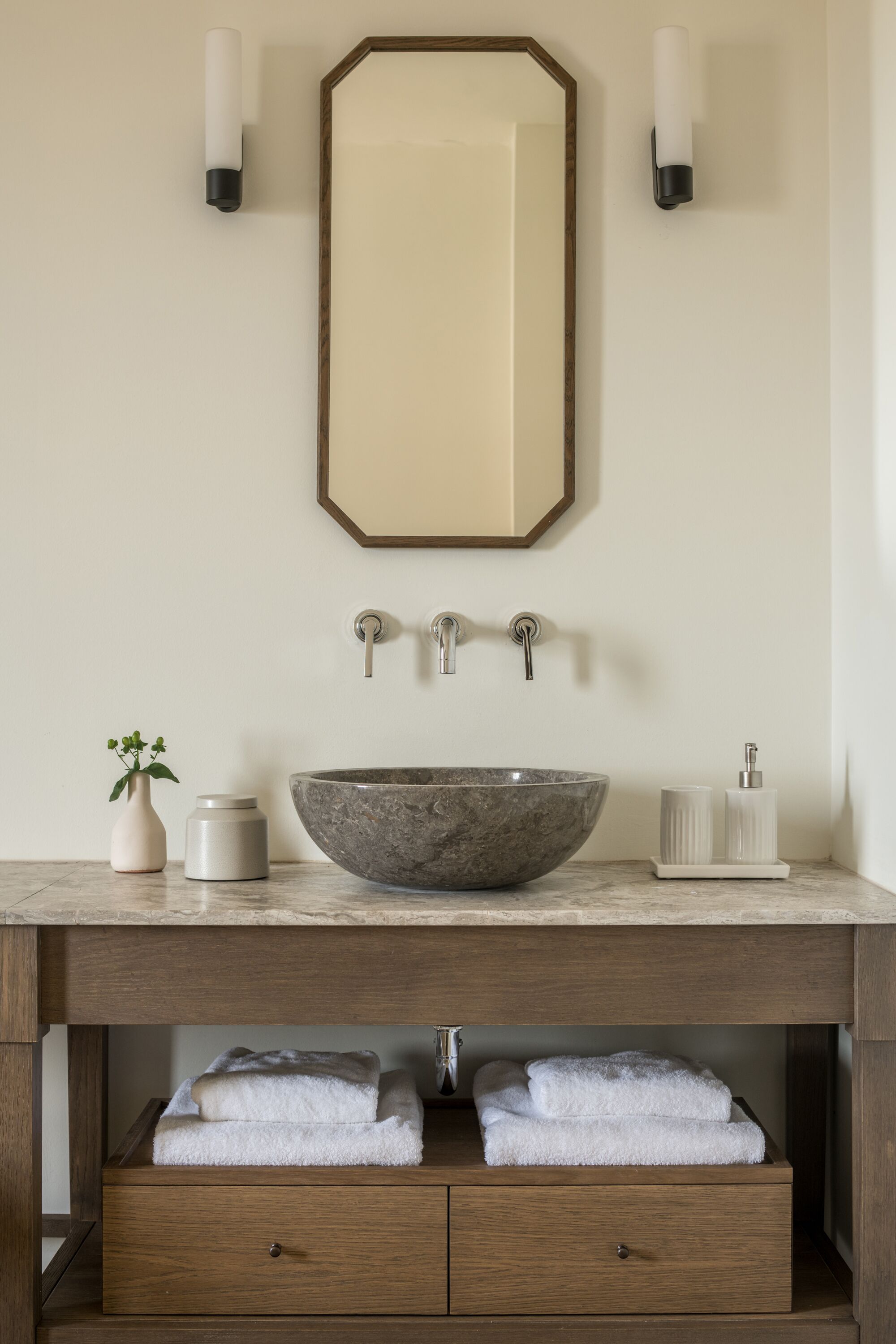Un bagno con un grande specchio, un lavabo in pietra, due cassetti per asciugamani e una piccola pianta.