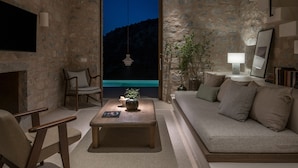 A modern living room with a stone wall, a sofa, a coffee table, and a TV. - Monolithoi Villas Mani (West Mani)