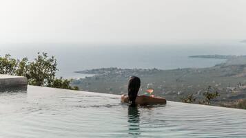 A person relaxing in a infinity pool with a glass of wine, overlooking a coastal landscape.