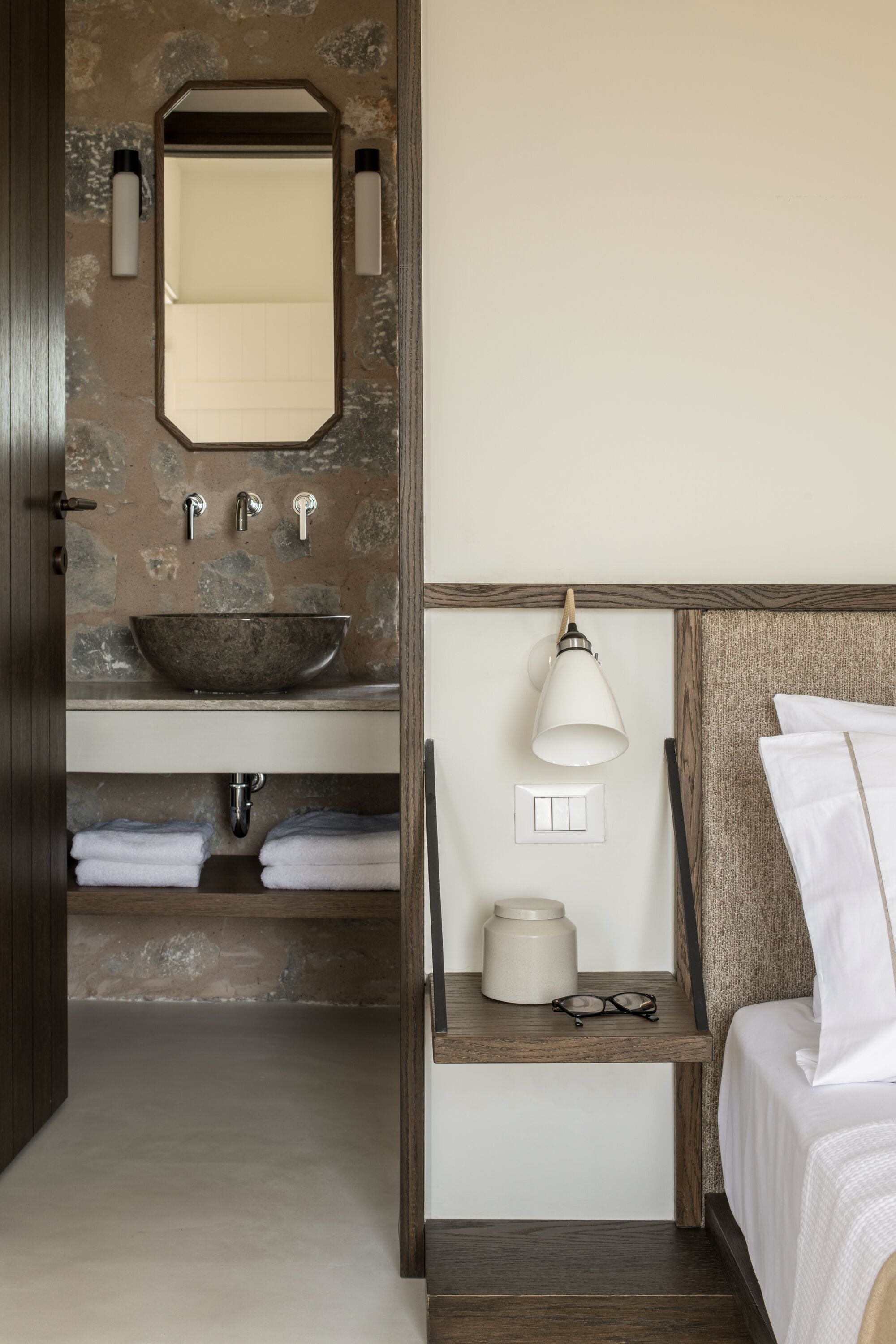 Une salle de bain avec un lavabo en pierre, un miroir et une table de chevet avec une lampe et des lunettes.