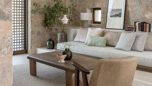 A cozy living room with a stone wall, a sofa with cushions, a wooden coffee table, a vase with a plant, a hanging lamp, and a framed picture on the wall. - Monolithoi Villas Mani (West Mani)