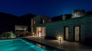 A modern house with a swimming pool, stone walls, and a patio area with outdoor lighting. - Monolithoi Villas Mani (West Mani)