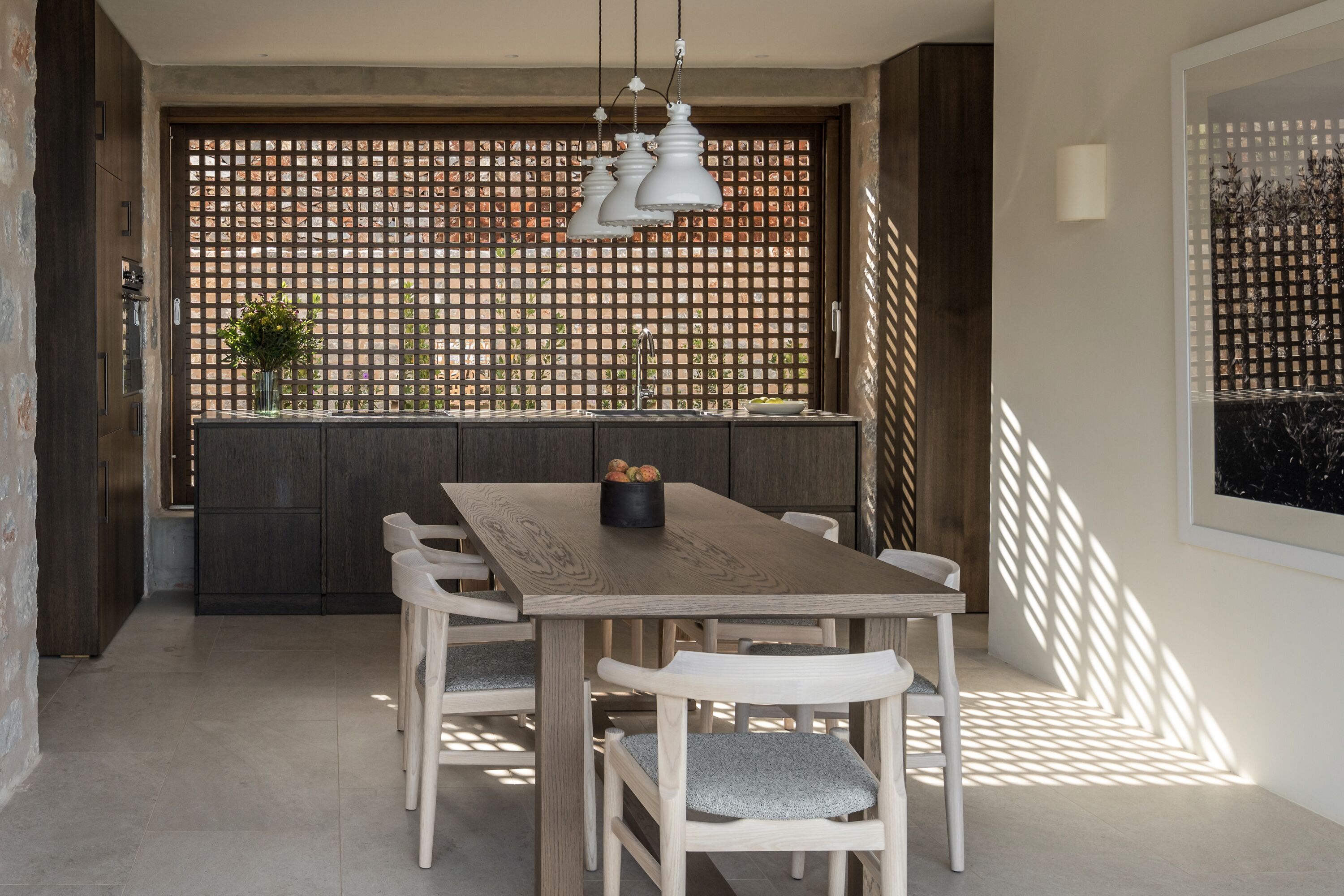 Un espace repas avec une table et des chaises en bois, un mur décoratif et des luminaires suspendus.