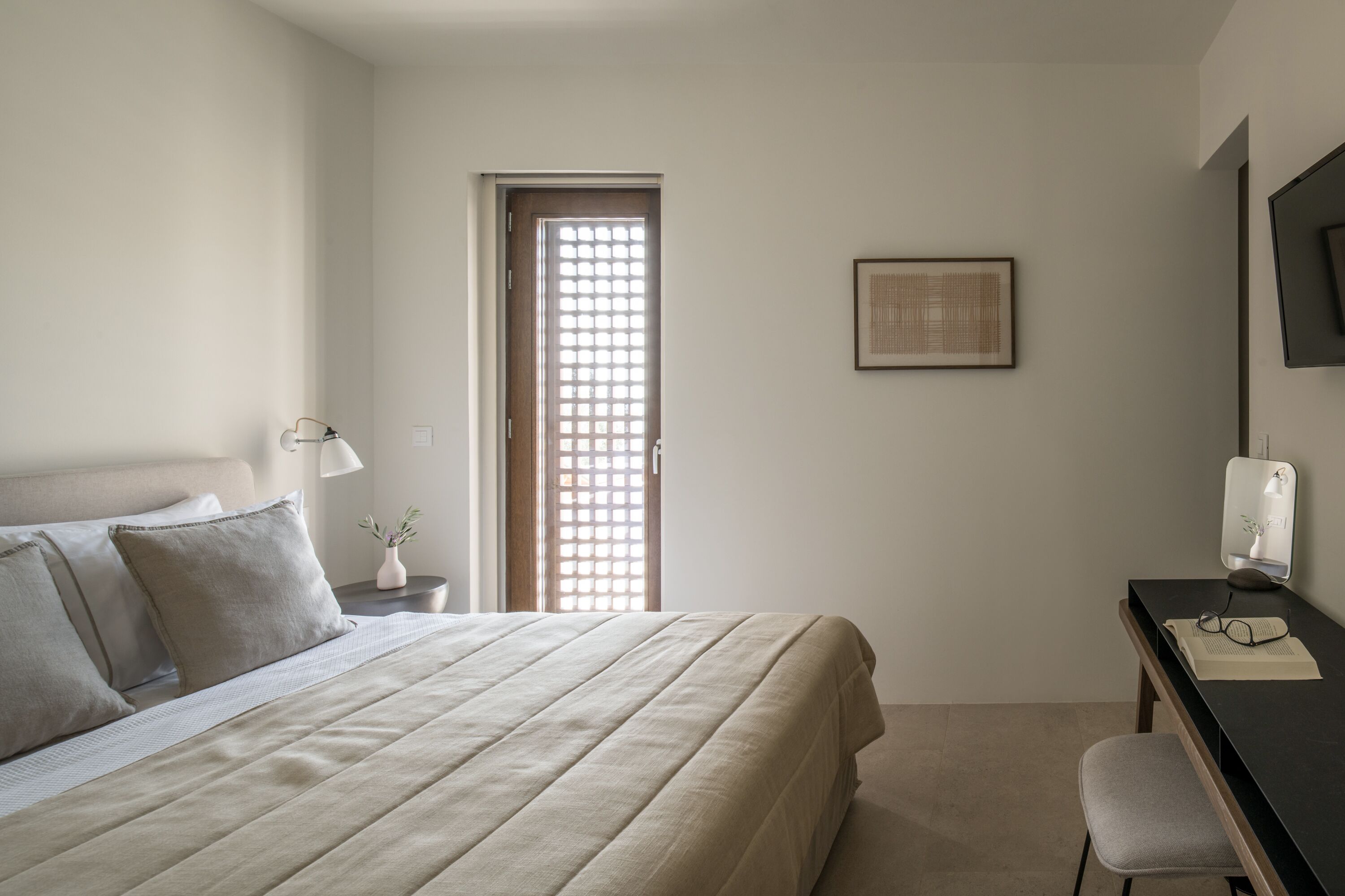 A bedroom with a bed, bedside table, desk, chair, and a door with a window.