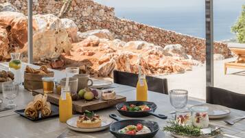 Una mesa preparada para una comida con diversos platos, bebidas y una vista panorámica del mar y las rocas.