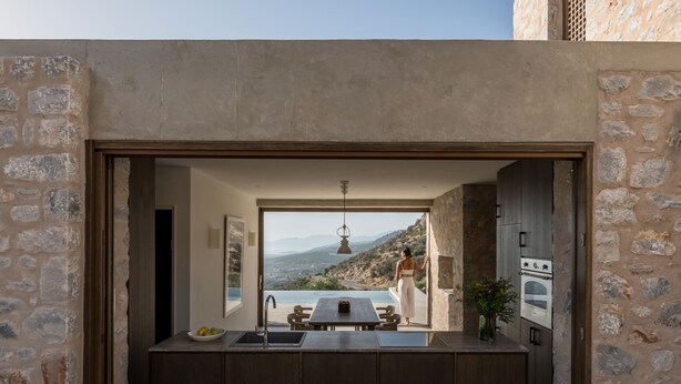 A modern kitchen with a stone wall, a large window, and a view of a mountainous landscape. - Monolithoi Villas Mani (West Mani)