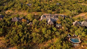 Vue aérienne d’un complexe hôtelier composé de plusieurs chalets aux toits de chaume, entourés d’une forêt dense.