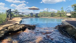 Une piscine avec une terrasse en bois, deux chaises longues et un parasol.