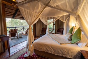 Un dormitorio con una cama grande, una silla de madera, una mesita y un balcón con vistas a árboles.