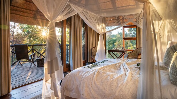 Une chambre à coucher avec un lit à baldaquin, une terrasse en bois et une vue sur les arbres.