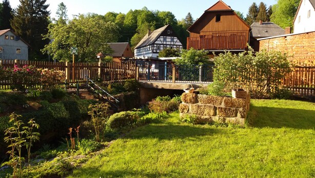 Un village européen traditionnel, avec des bâtiments en pierre, un pont en bois et un jardin bien entretenu.