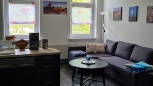 Un salon moderne avec un canapé, une table basse et un coin cuisine équipé d’une machine à café et d’un panier.