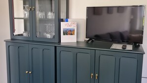Un meuble en bois bleu foncé, doté d’étagères à façade vitrée où sont exposés des objets en verre transparent, un tableau encadré accroché au mur et un téléviseur à écran plat posé sur le dessus.