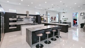 Une cuisine moderne dotée d’un grand îlot central, de meubles de couleur sombre et d’appareils électroménagers en acier inoxydable.