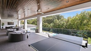 Un espace de vie extérieur comprenant une table de ping-pong, des sièges et une vue sur la piscine.