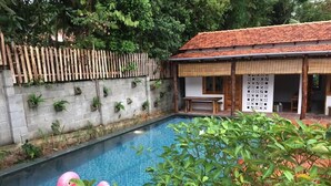 A swimming pool with a pink flamingo float, surrounded by greenery and a wooden fence. - Langchia Hostel & Bar (Phu Quoc)