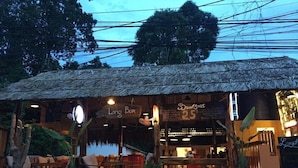 A restaurant with a thatched roof, outdoor seating, and a sign indicating a breakfast menu priced at $2.5. - Langchia Hostel & Bar (Phu Quoc)