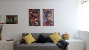 Un salon avec un canapé gris, deux coussins, une petite table, un panier et une lampe.