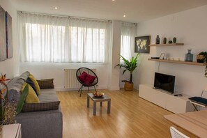 A living room with a sofa, a chair, a coffee table, a TV, and shelves with decorative items. - APARTMENTS BCN CENTRAL-MONTJUIC (Barcelona)