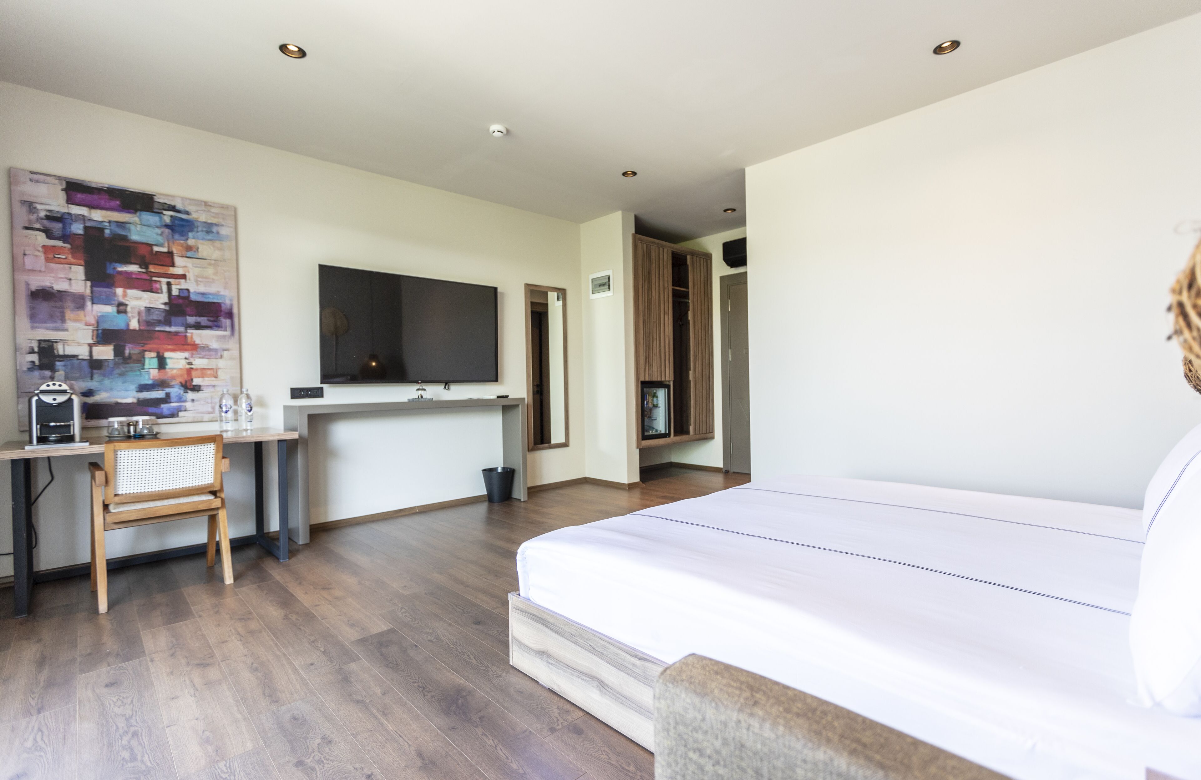 A modern hotel room with a large bed, a desk with a chair, a flat-screen TV, and a wooden floor.