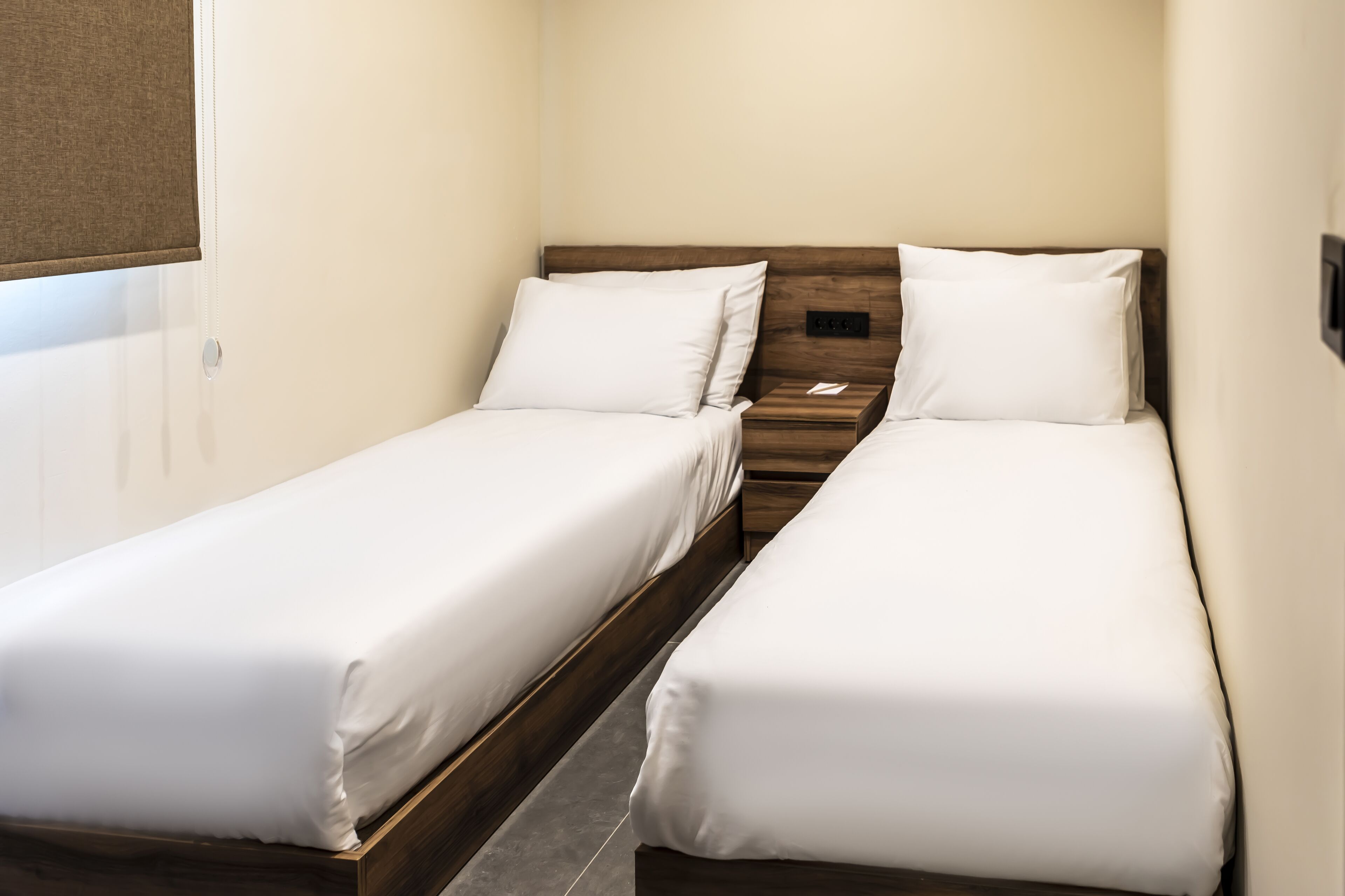 Una habitación pequeña y limpia con dos camas individuales, un cabecero de madera y una mesita de noche de madera con una lámpara.