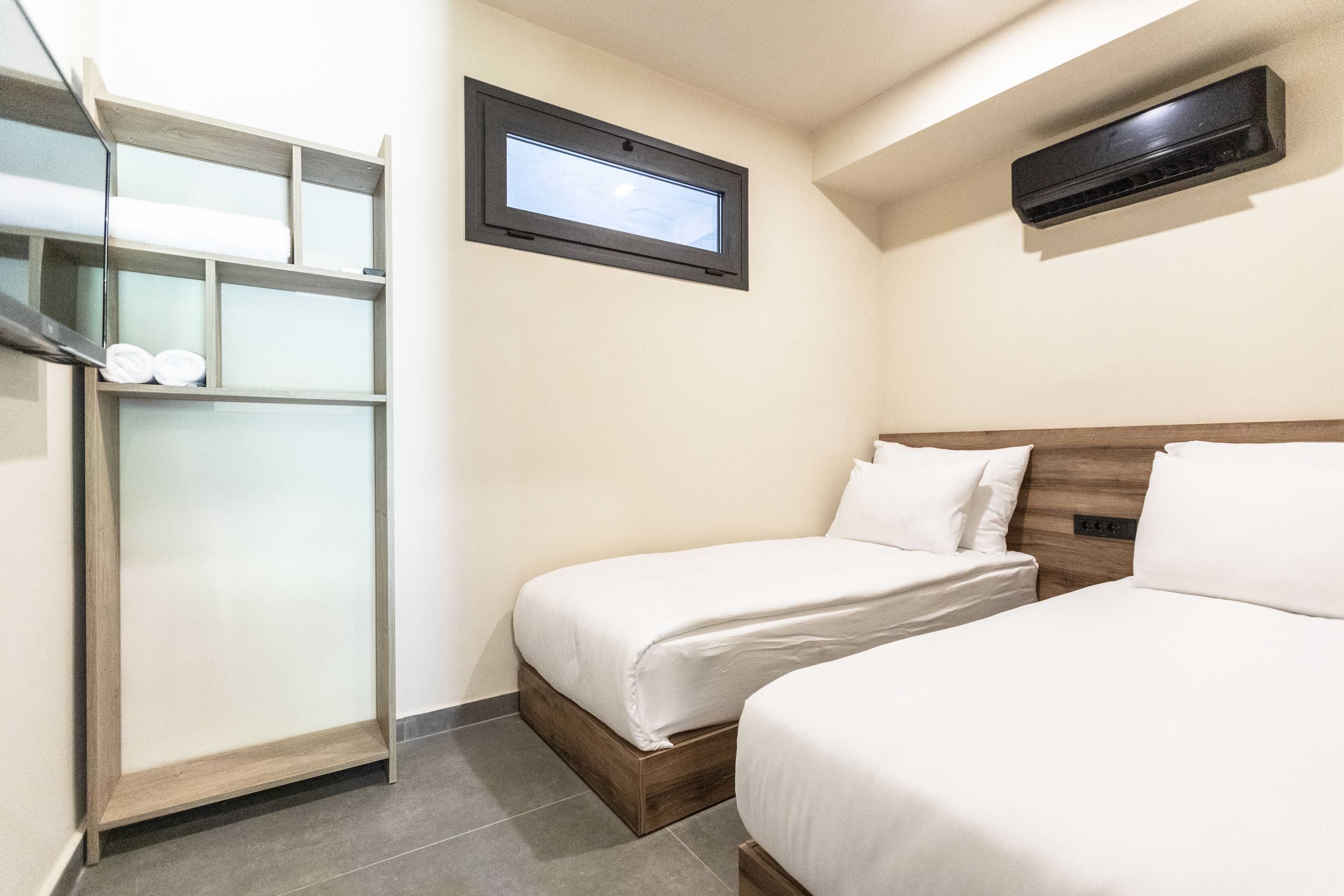 Habitación de hotel con dos camas, un armario, una ventana y un equipo de aire acondicionado.