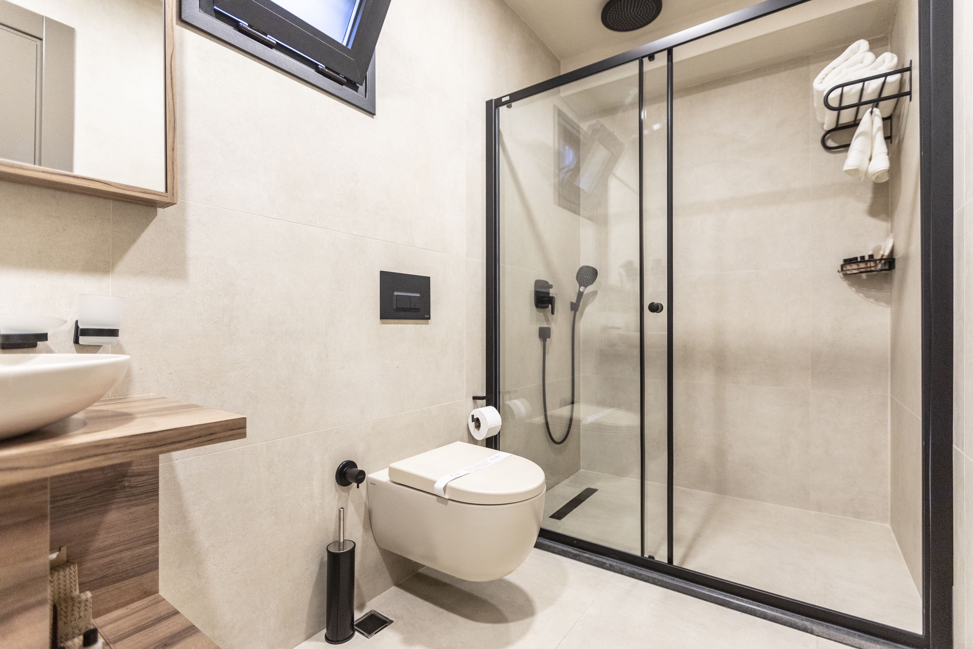 A modern bathroom with a glass-enclosed shower, a toilet, and a sink with a wooden countertop.