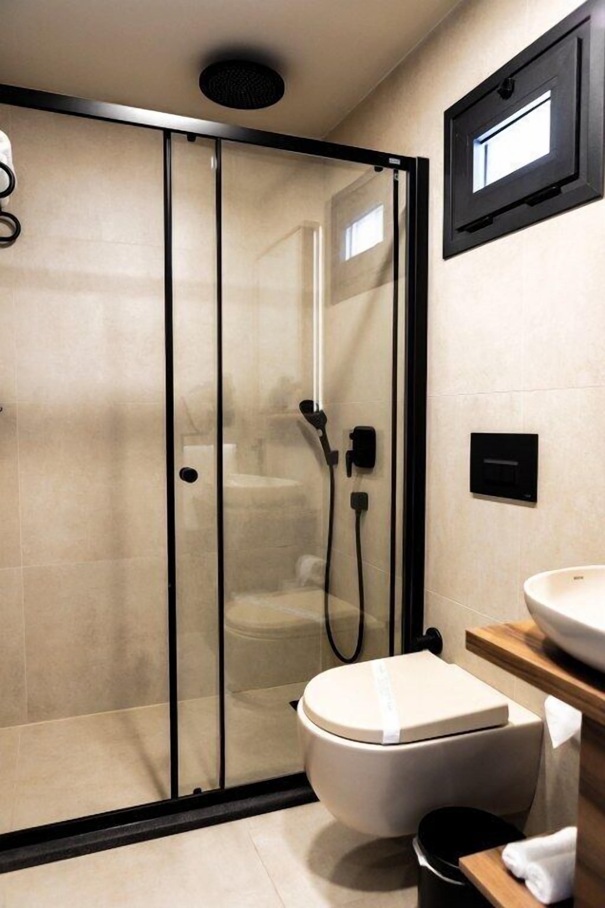 Un baño moderno con ducha envuelta en vidrio, inodoro y lavamanos con espejo.