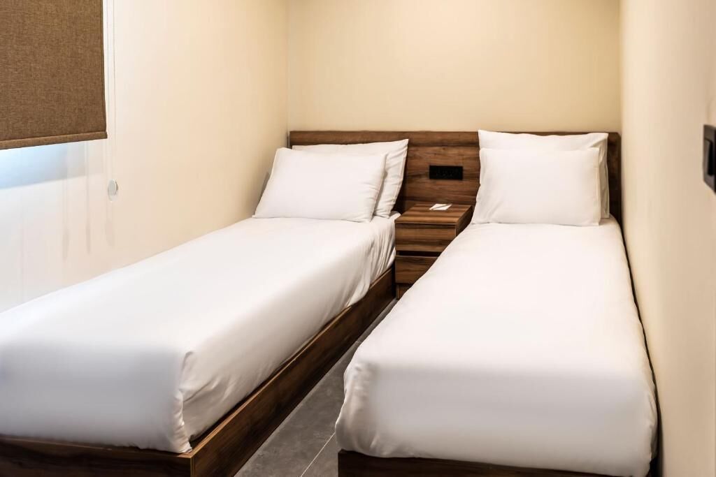 A small, compact room with two single beds, each with white bedding and wooden headboards.