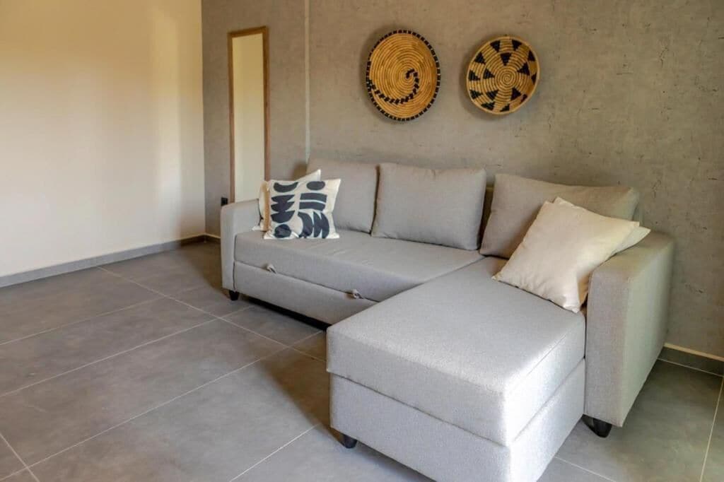 Un salon moderne avec un canapé d’angle gris, deux éléments décoratifs muraux et un mur sobre.
