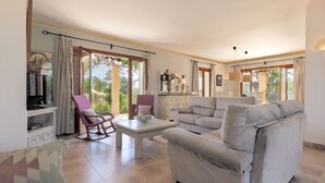 Un salon spacieux comprenant un canapé, un fauteuil et une table basse. On y trouve également un téléviseur et un meuble contenant des objets décoratifs.