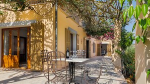 Une cour avec une table et des chaises, une porte et un bâtiment doté de volets.