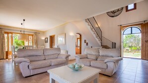 Un salon spacieux avec deux canapés beige, une table basse blanche et un escalier menant à un espace extérieur.