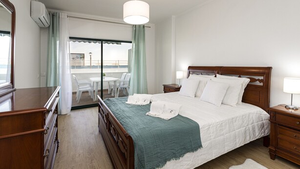 Quarto de hotel com cama de madeira, escrivaninha, cadeira e varanda com vista.