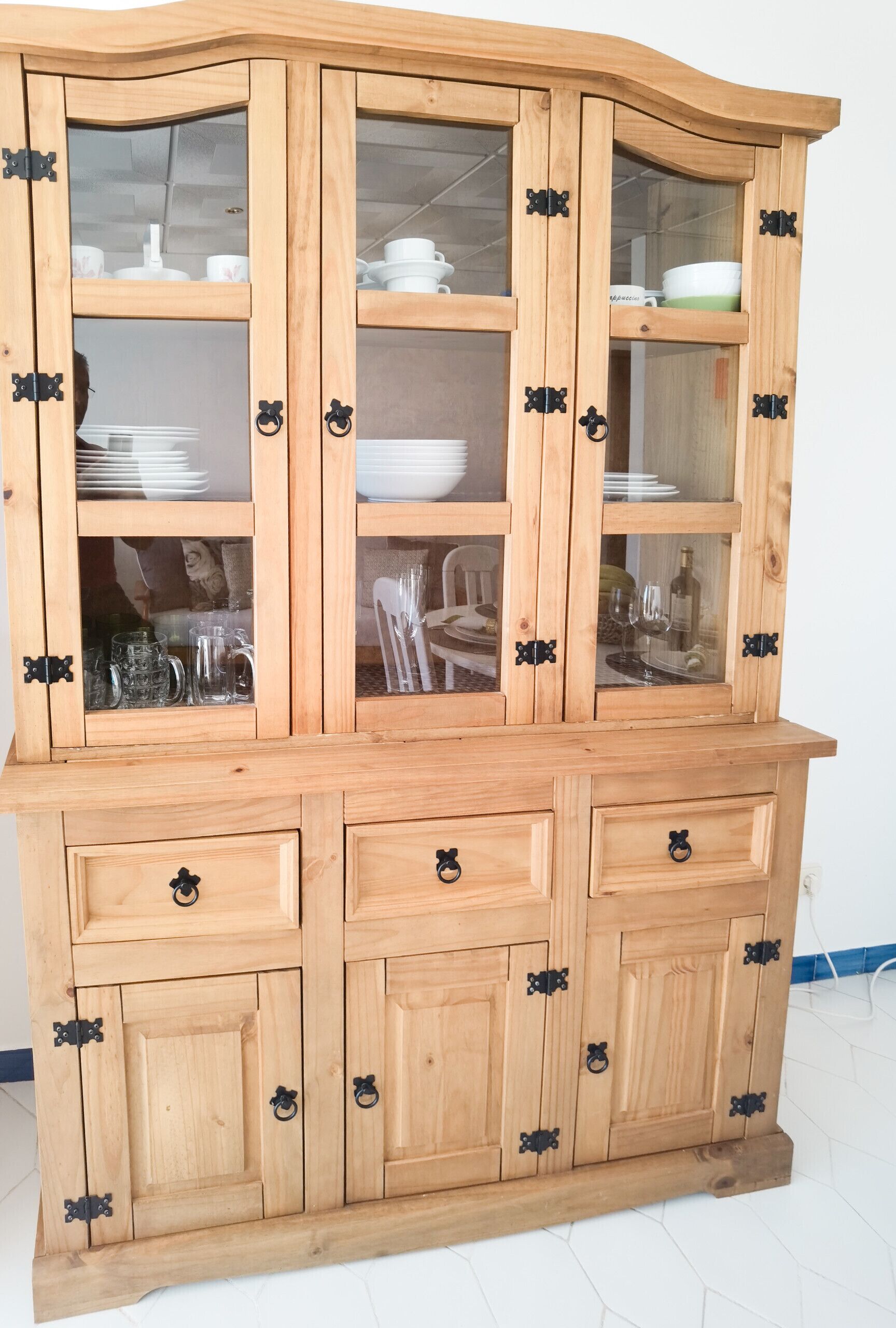 A wooden cabinet with glass doors and black handles, containing various dishes and glassware.