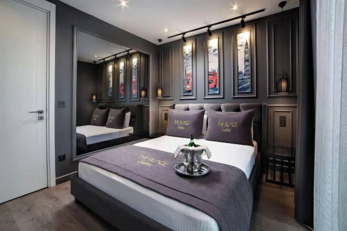 A modern bedroom with a large bed, a mirror, artwork on the walls, and a small table with a decorative item.