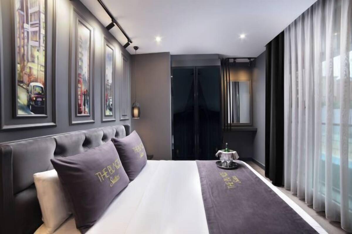 A modern hotel room with a large bed, dark curtains, a cityscape view, and a small table with a tray.