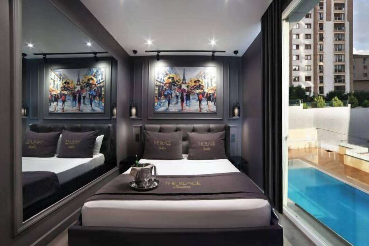 A modern hotel room with a large bed, two wall-mounted paintings, a view of a swimming pool, and a balcony.