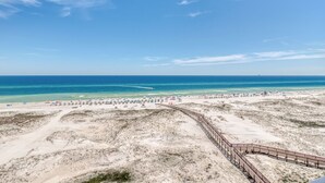 Ein Strand mit einer Holzpromenade, die zum Ufer führt, Sanddünen und einem strahlend blauen Himmel.