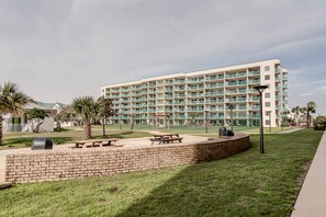 Un hotel de varios pisos con piscina, mesas de picnic y un muro de ladrillo.