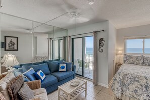 Un salón amplio con un sofá azul, una mesa de centro de madera, un espejo grande y un balcón con vistas al mar.