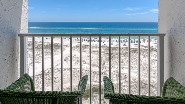 Ein Balkon mit Korbstühlen mit Blick auf einen Strand und einen klaren, blauen Himmel.